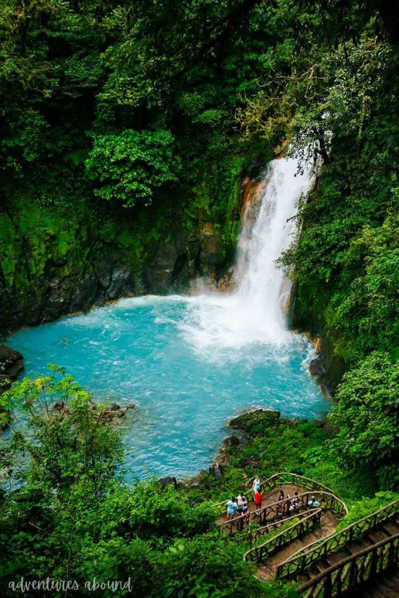 A vibrant waterfall pouring into a blue river surrounded by lush jungle.