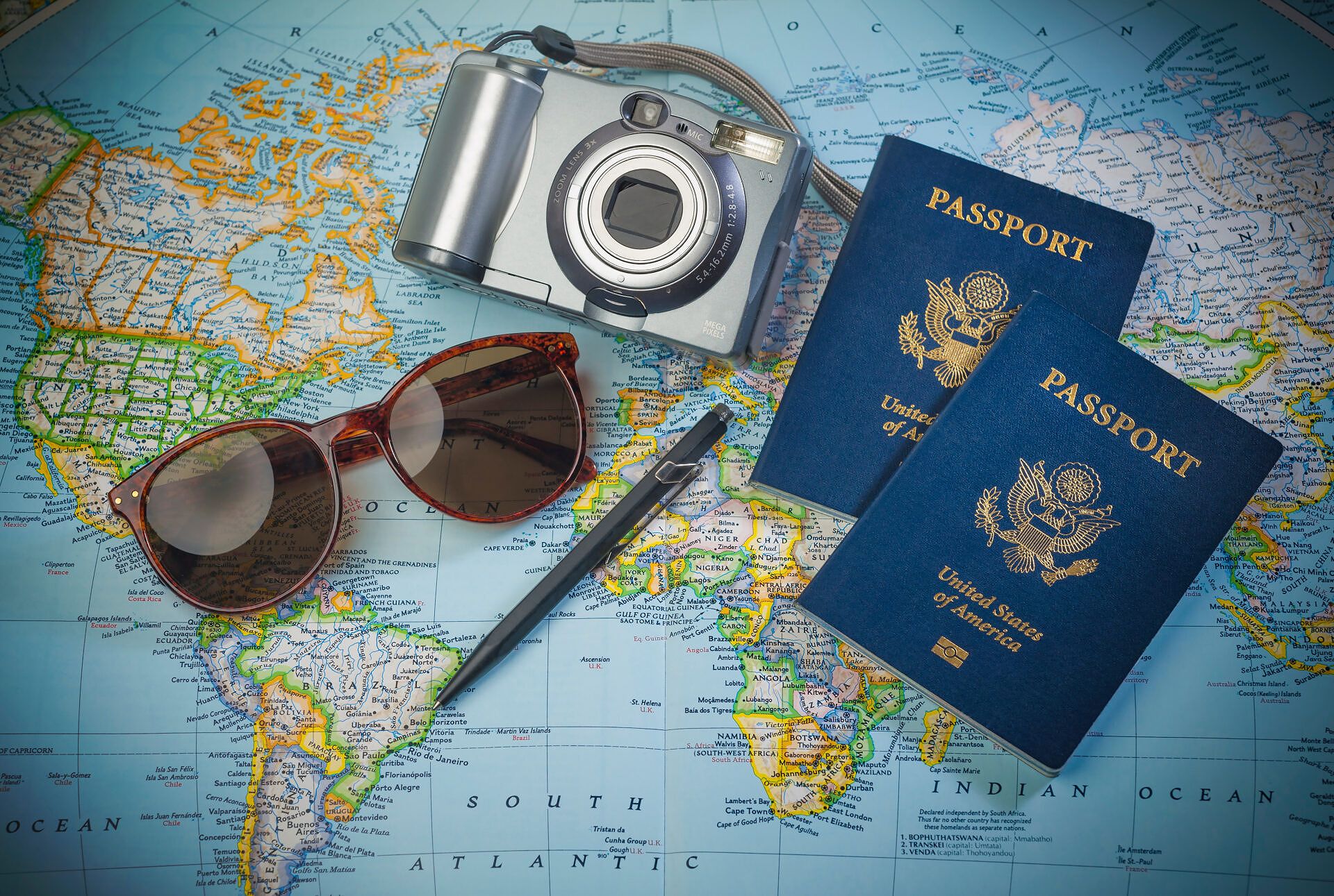 Passports, camera and sunglasses flat lay on world map